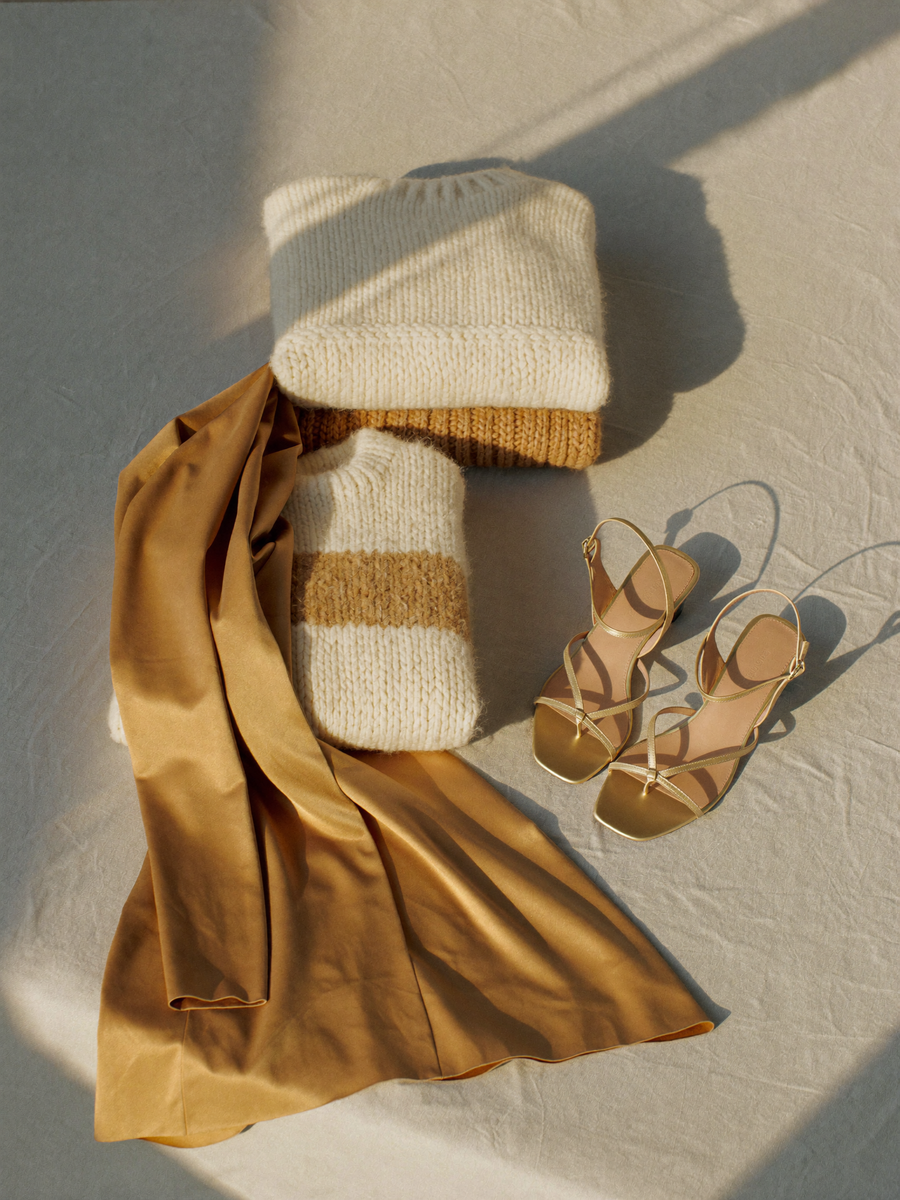 Folded knit sweaters, satin dress, and leather sandals in warm morning light